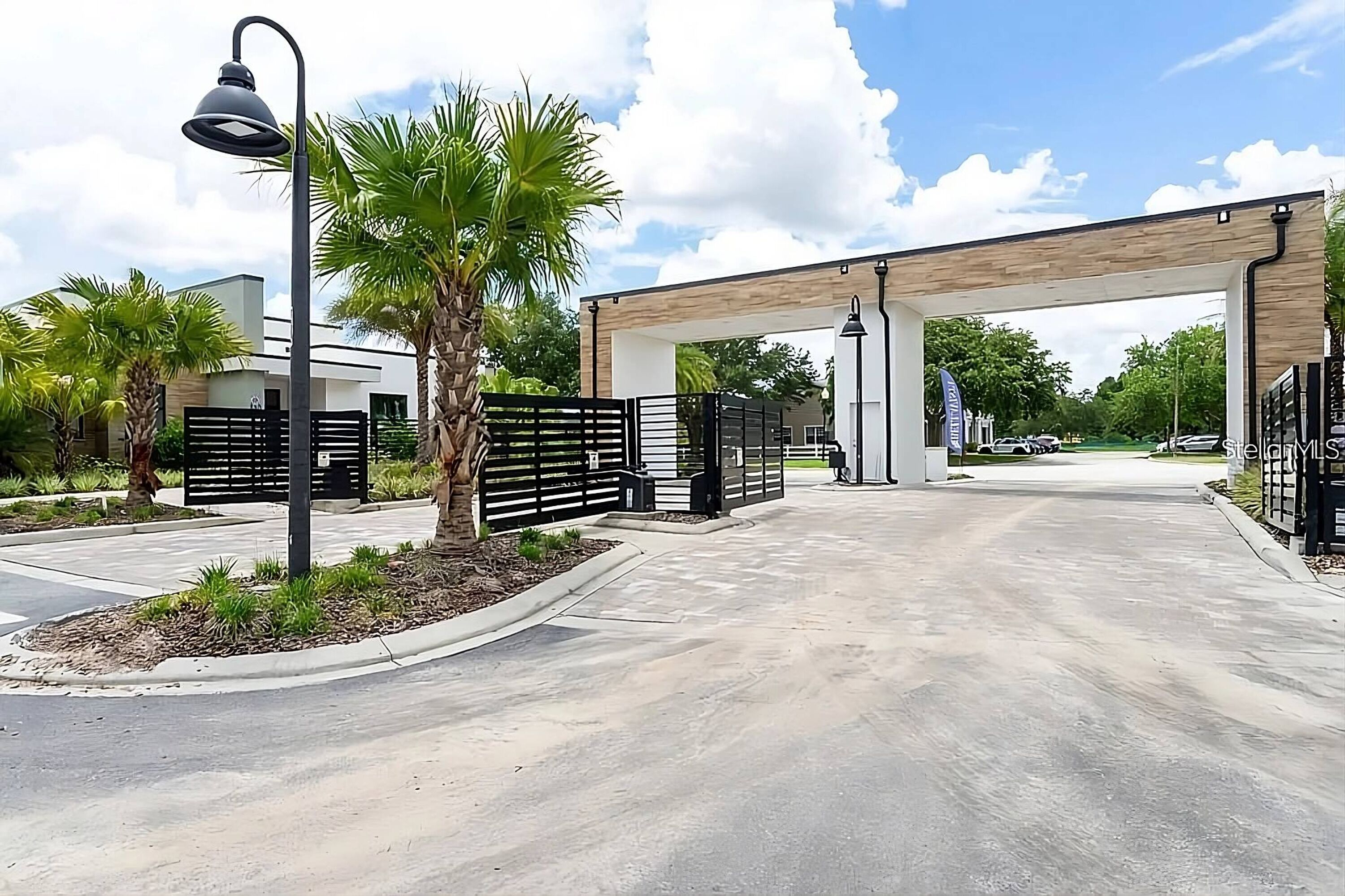 A gated entrance with a modern design, palm trees, and a clear sky.