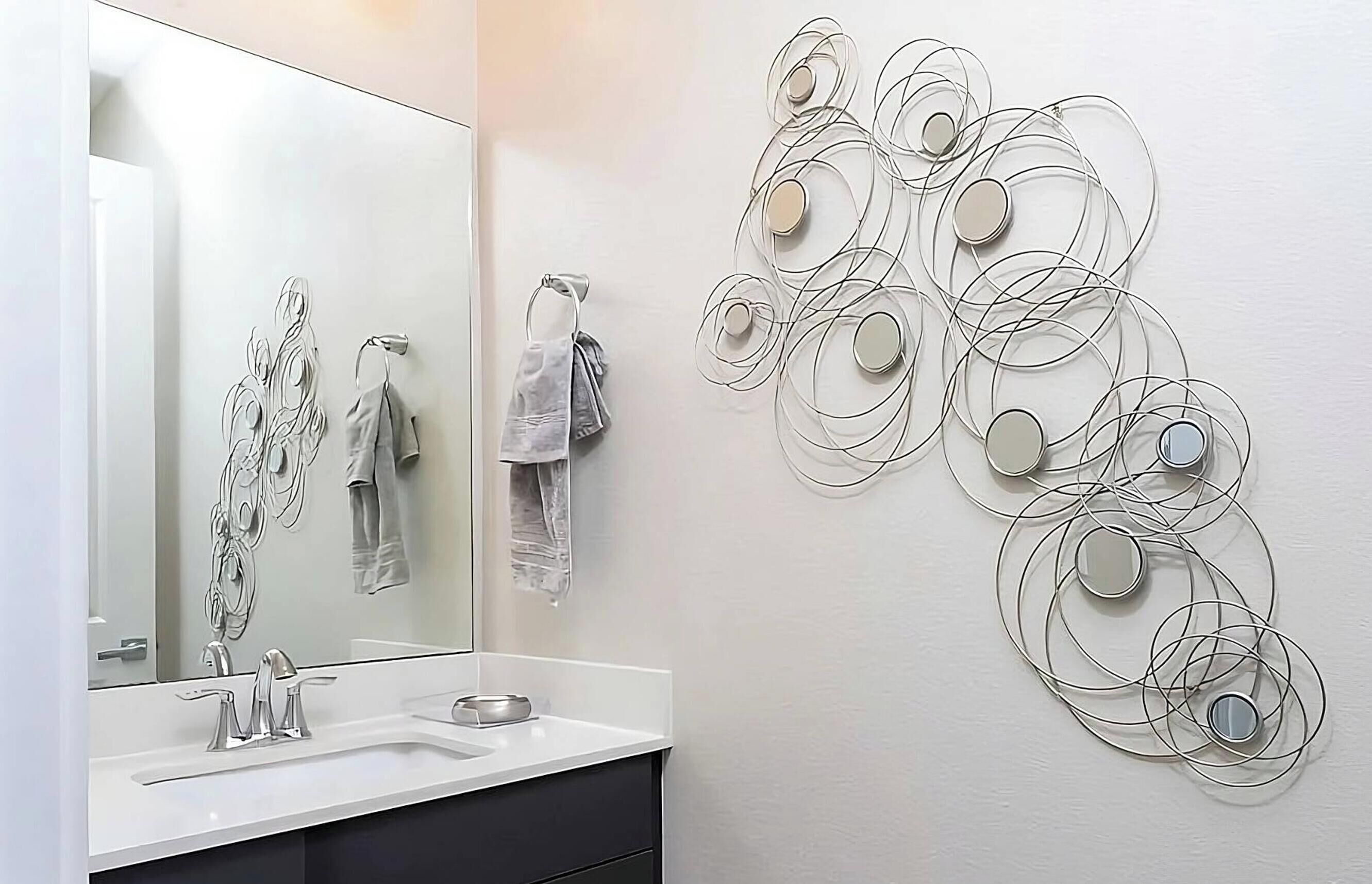 Une salle de bain moderne avec un grand miroir, un lavabo blanc et un porte-serviettes fixé au mur.