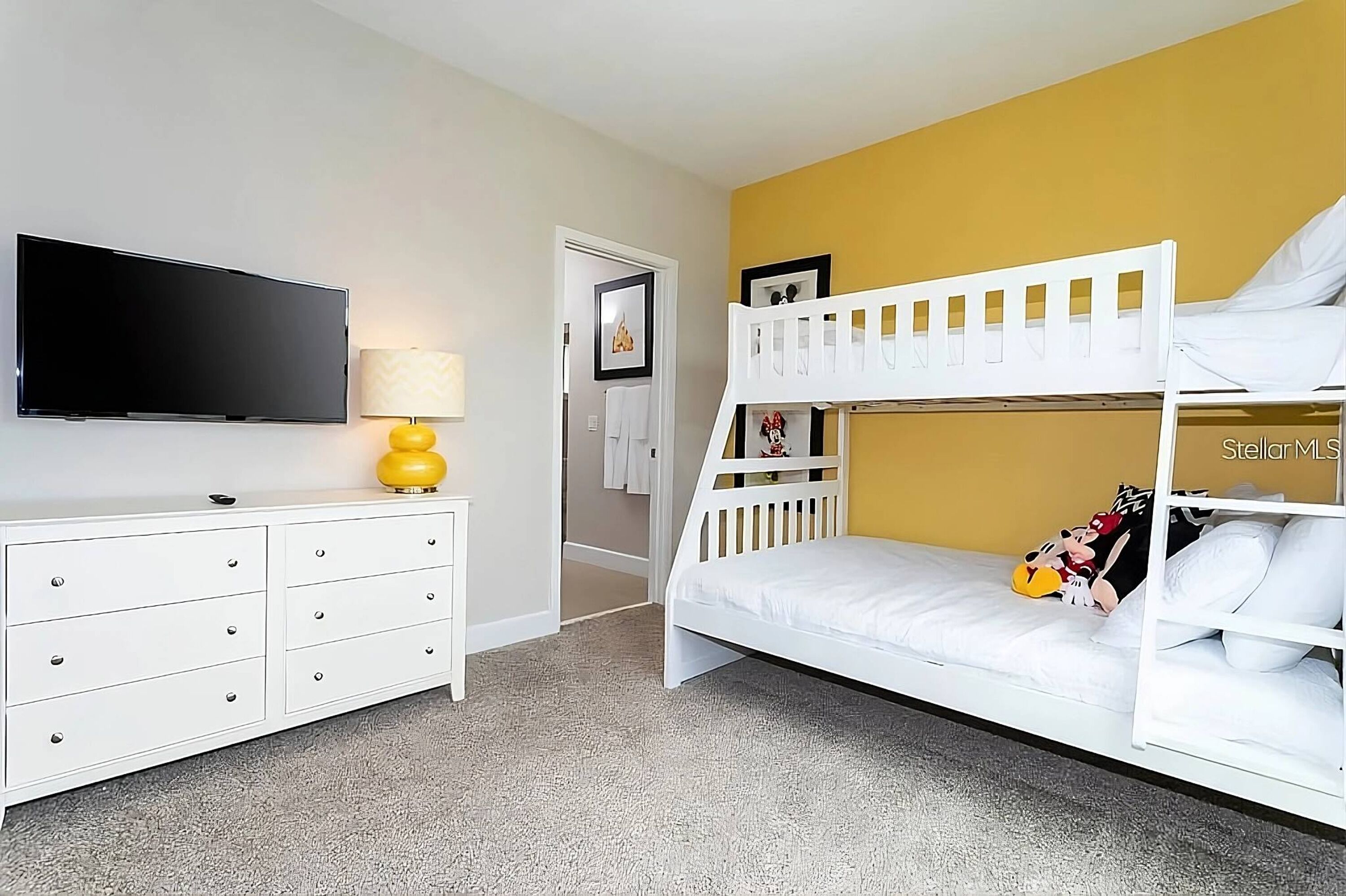 A room with a bunk bed, a flat-screen TV, a white dresser, and a yellow lamp.