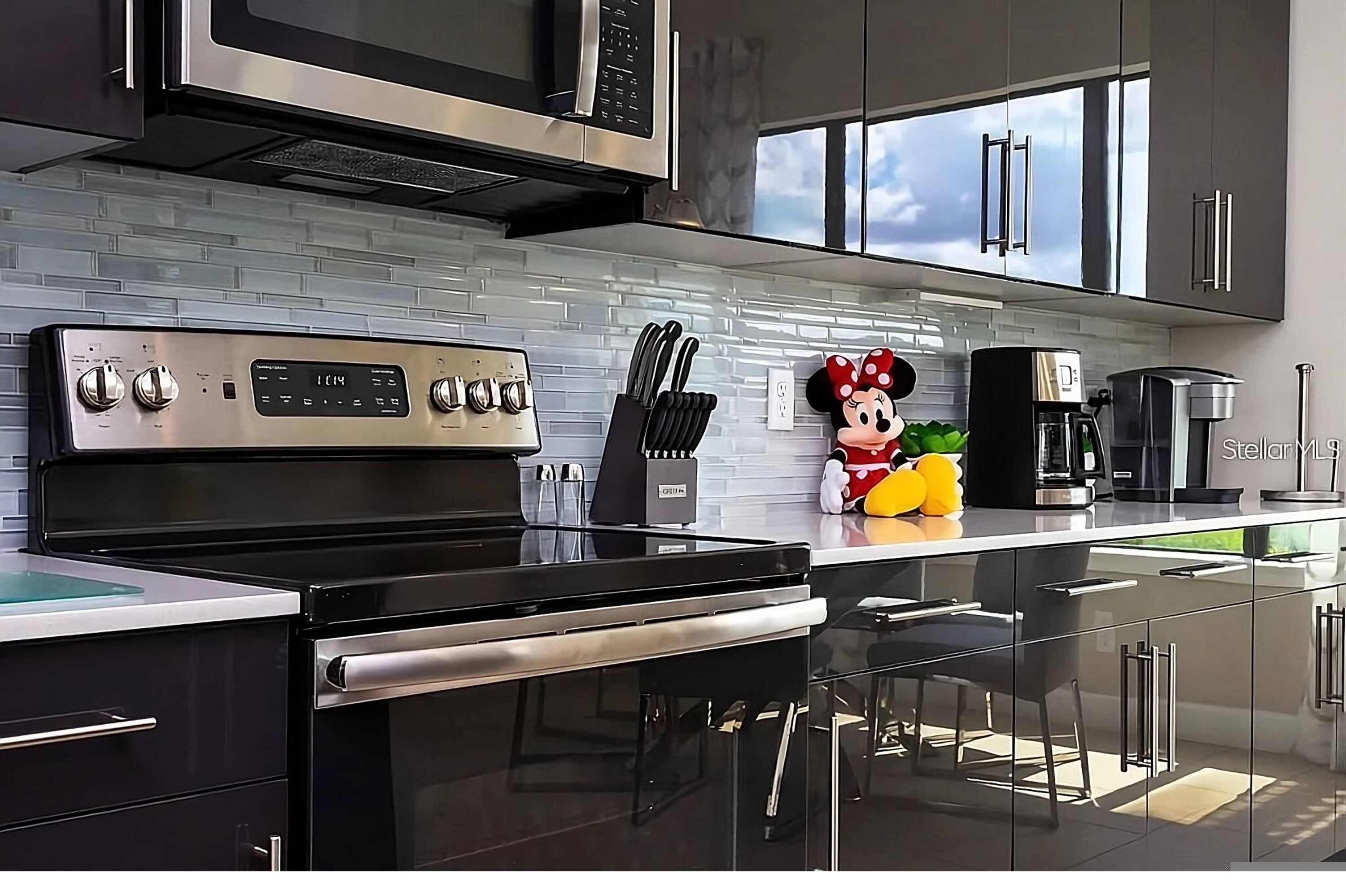 A modern kitchen with stainless steel appliances, a black stove, and a Minnie Mouse decoration.