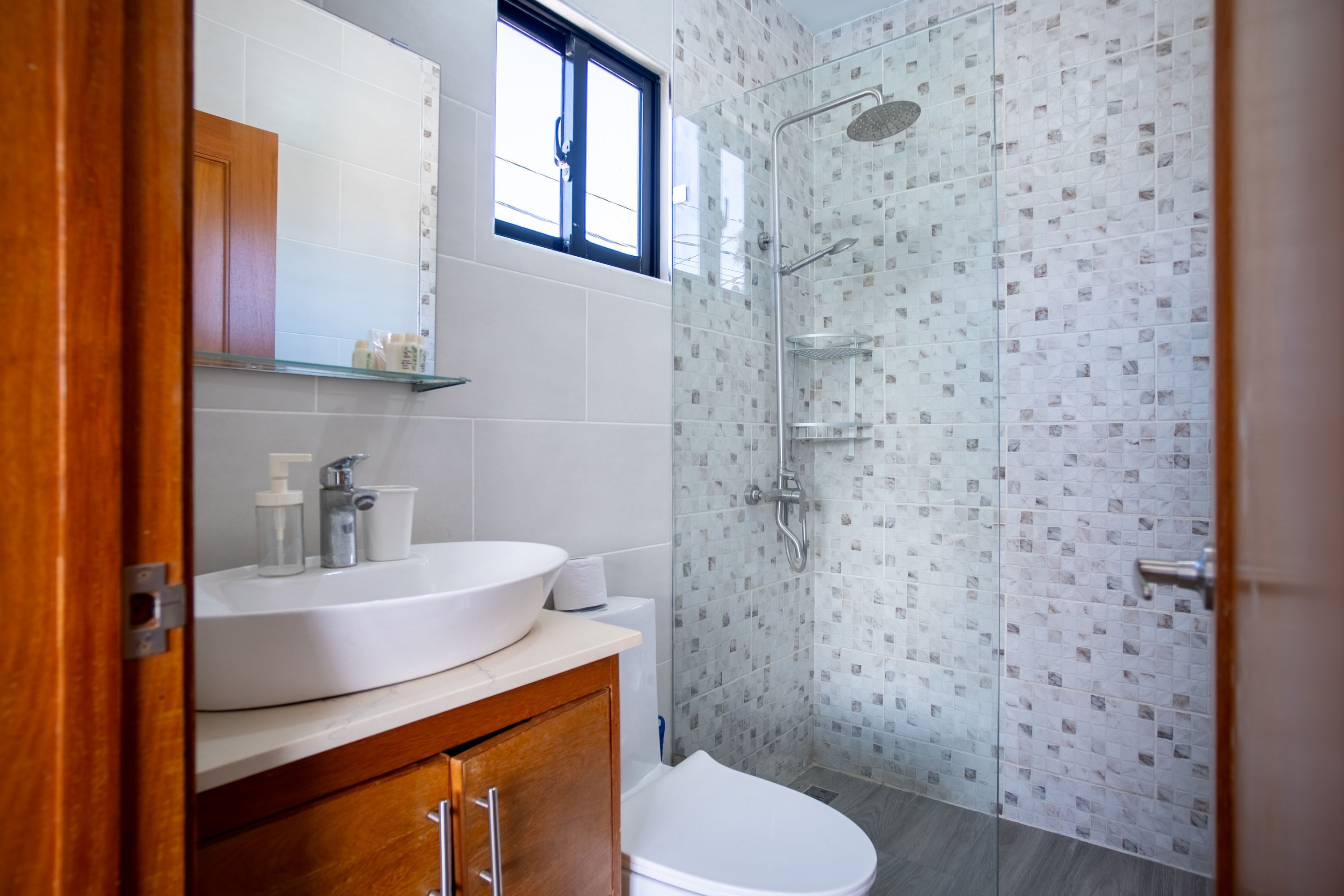 Un baño moderno con lavamanos blanco, espejo y cabina de ducha de vidrio.