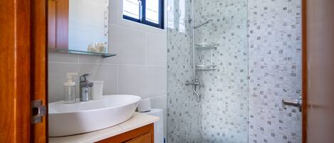 Un baño moderno con lavamanos blanco, espejo y cabina de ducha de vidrio.