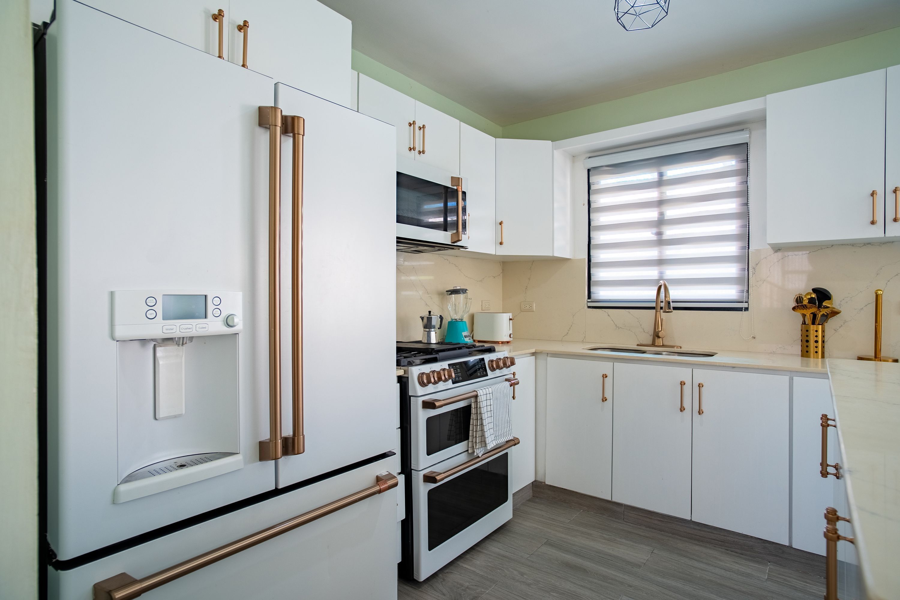 Cucina con mobili bianchi, forno a incasso, microonde e dispenser per l'acqua.