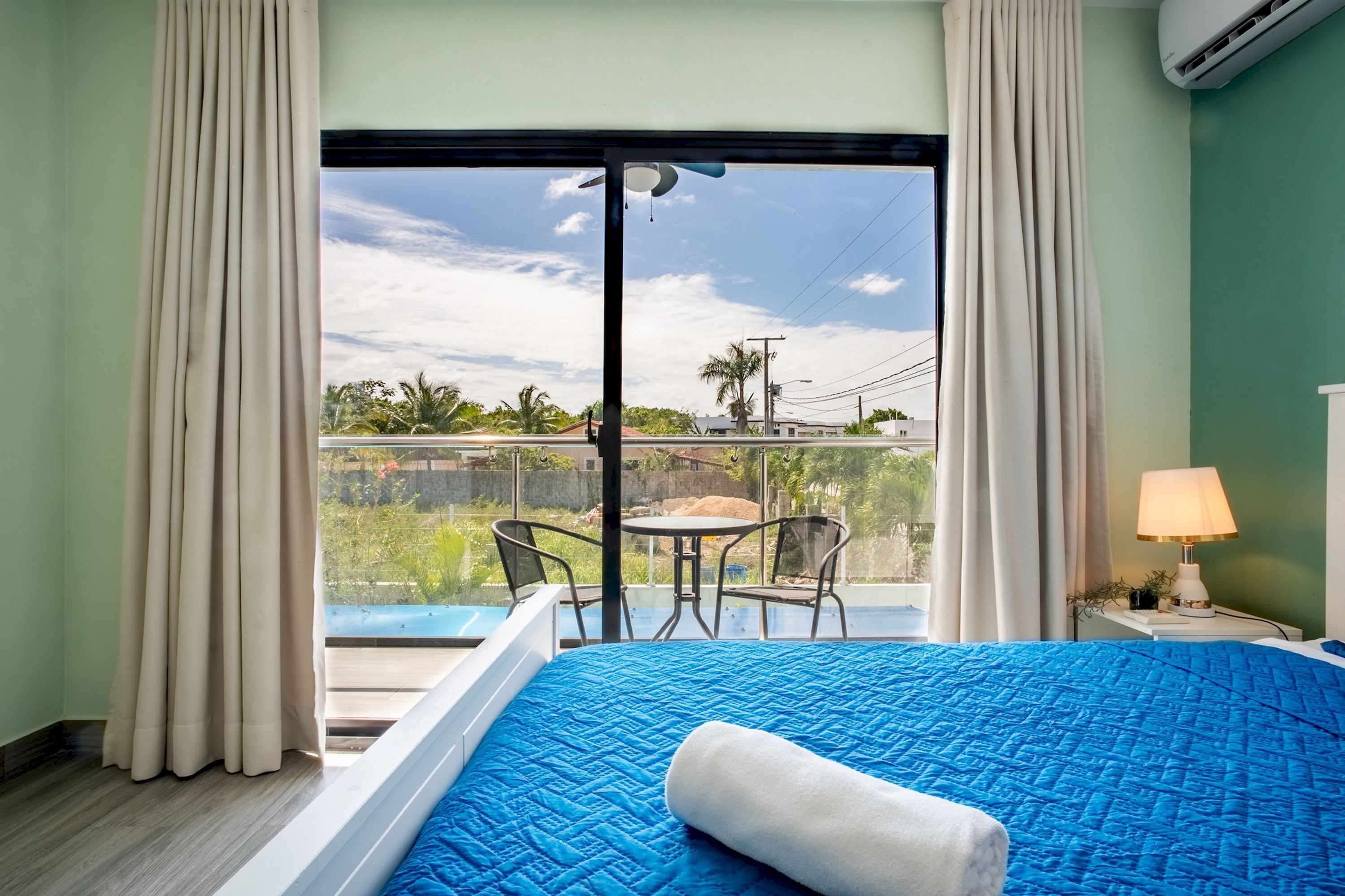 A hotel room with a bed, a balcony with a table and chairs, and a view of the outside.