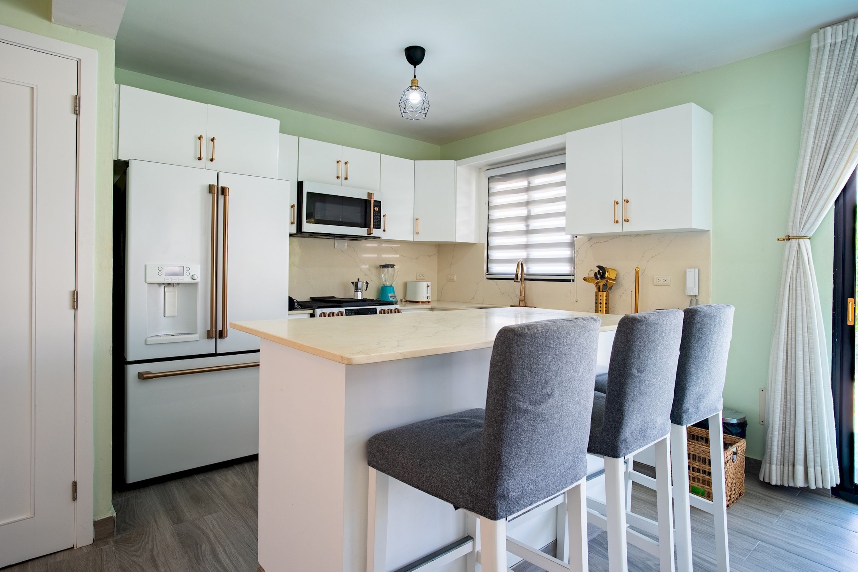 A modern kitchen with white cabinets, a microwave, a refrigerator, and a bar area with grey chairs.