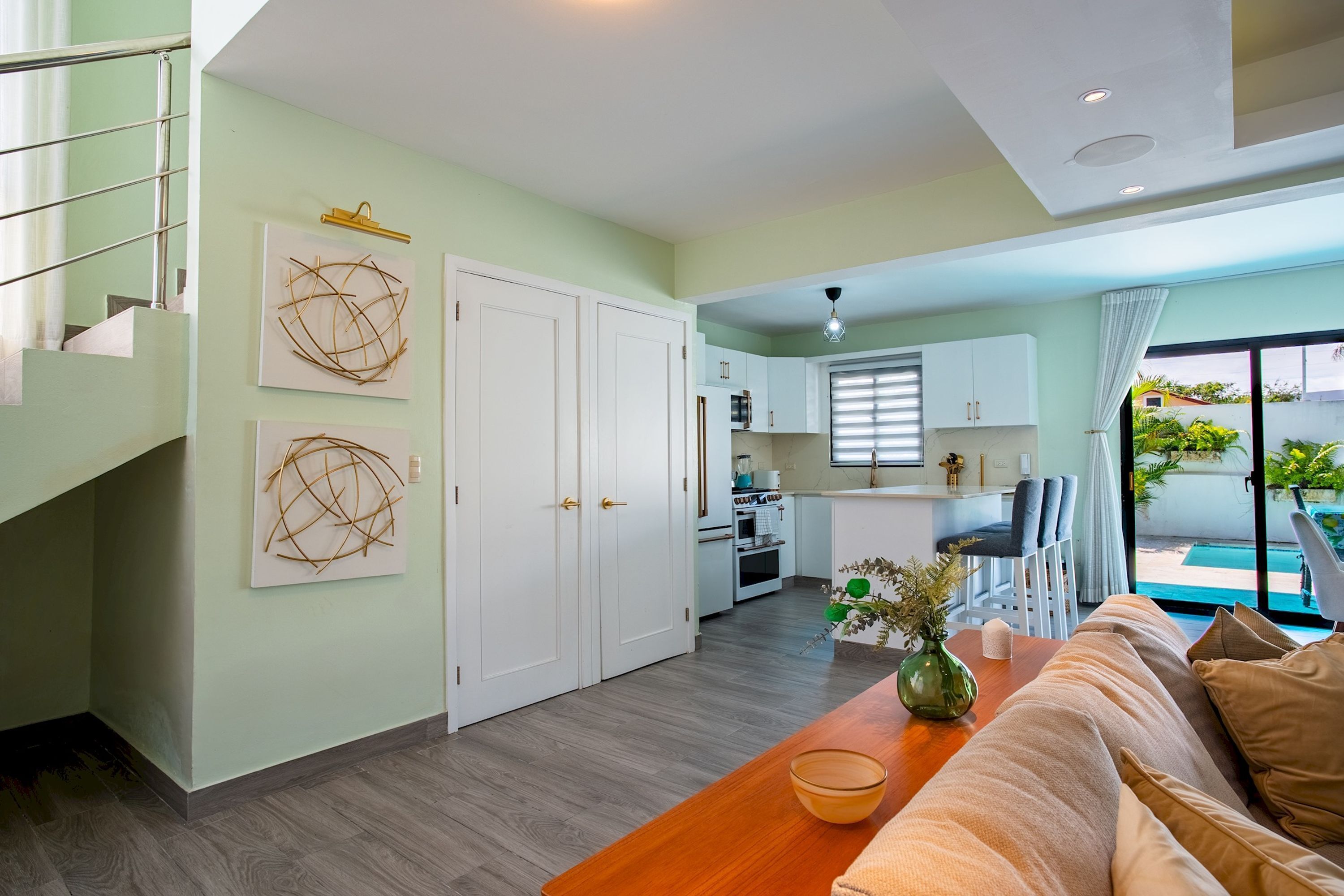 A modern interior with a staircase, a dining area with a wooden table, and a kitchen in the background.