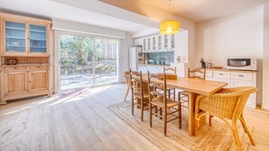 A spacious kitchen with a dining area, wooden cabinets, and a large window. - La Villa Pylataise – Pyla sur mer- Swimming pool (Pyla sur Mer)