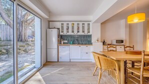 A modern kitchen with white cabinets, a dishwasher, and a dining area with a wooden table and chairs. - La Villa Pylataise – Pyla sur mer- Swimming pool (Pyla sur Mer)