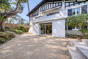 A modern two-story house with a gravel driveway, a stone wall, and a wooden fence. - La Villa Pylataise – Pyla sur mer- Swimming pool (Pyla sur Mer)