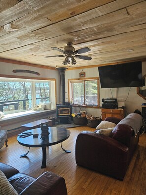 A cozy living room with a fireplace, a television, and a large window overlooking a lake.