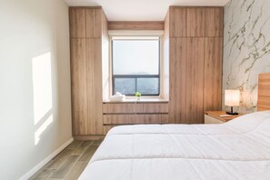 Een slaapkamer met een groot bed, een raam met uitzicht, houten lambrisering en een nachtkastje met een lamp.