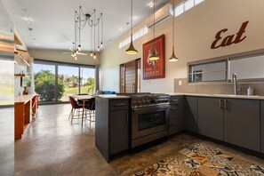 A modern kitchen with a large island, stainless steel appliances, pendant lighting, and a view of the outdoors. - Two bedroom  in Puerto Rico, Aguada (Aguada)