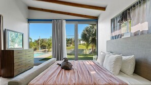 A bedroom with a bed, a dresser, and a view of a pool and greenery. - Two bedroom  in Puerto Rico, Aguada (Aguada)