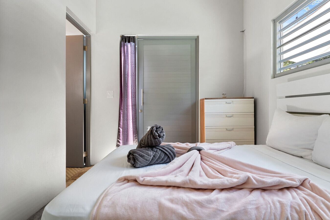 Une chambre à coucher avec un lit, une commode, une fenêtre avec des stores et une porte.