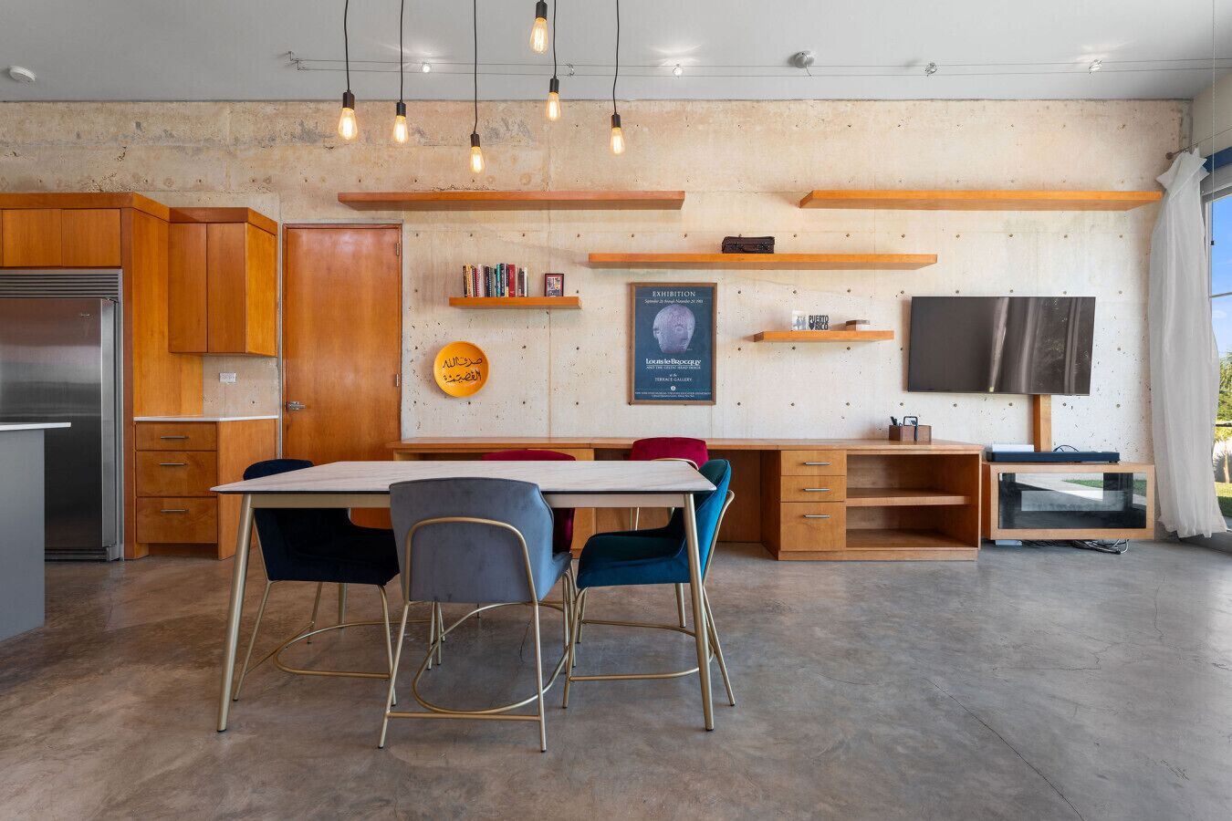 A modern kitchen with wooden cabinets, a dining table with chairs, a TV, and a poster on the wall.