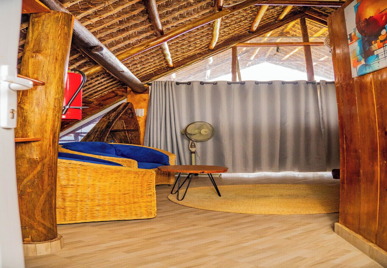 Ein Zimmer mit Holzboden, einem Korbsessel, einem kleinen Tisch und einem Ventilator.