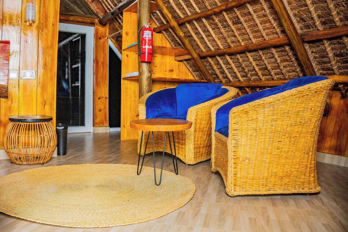Una habitación con techo de paja, muebles de mimbre, un tapete redondo y un extintor.