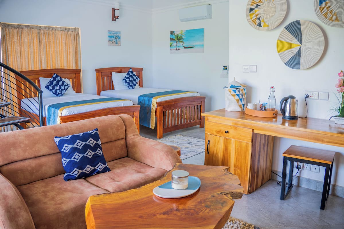 Habitación con dos camas, un sofá, un escritorio de madera y una mesita con una taza.