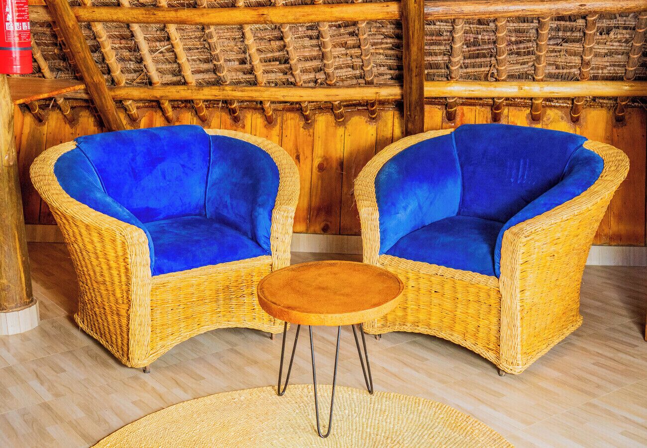 Two wicker chairs with blue cushions, a round wooden table, and a woven rug on a wooden floor.