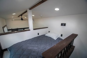 A single bed with a grey quilt, a wooden headboard, a ceiling fan, and a small wall-mounted light. - Busted Pallet (Anderson)