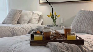 En seng med et bakkesæt med drikkevarer og et glas vand, en vase med gule blomster og en lampe på et natbord.