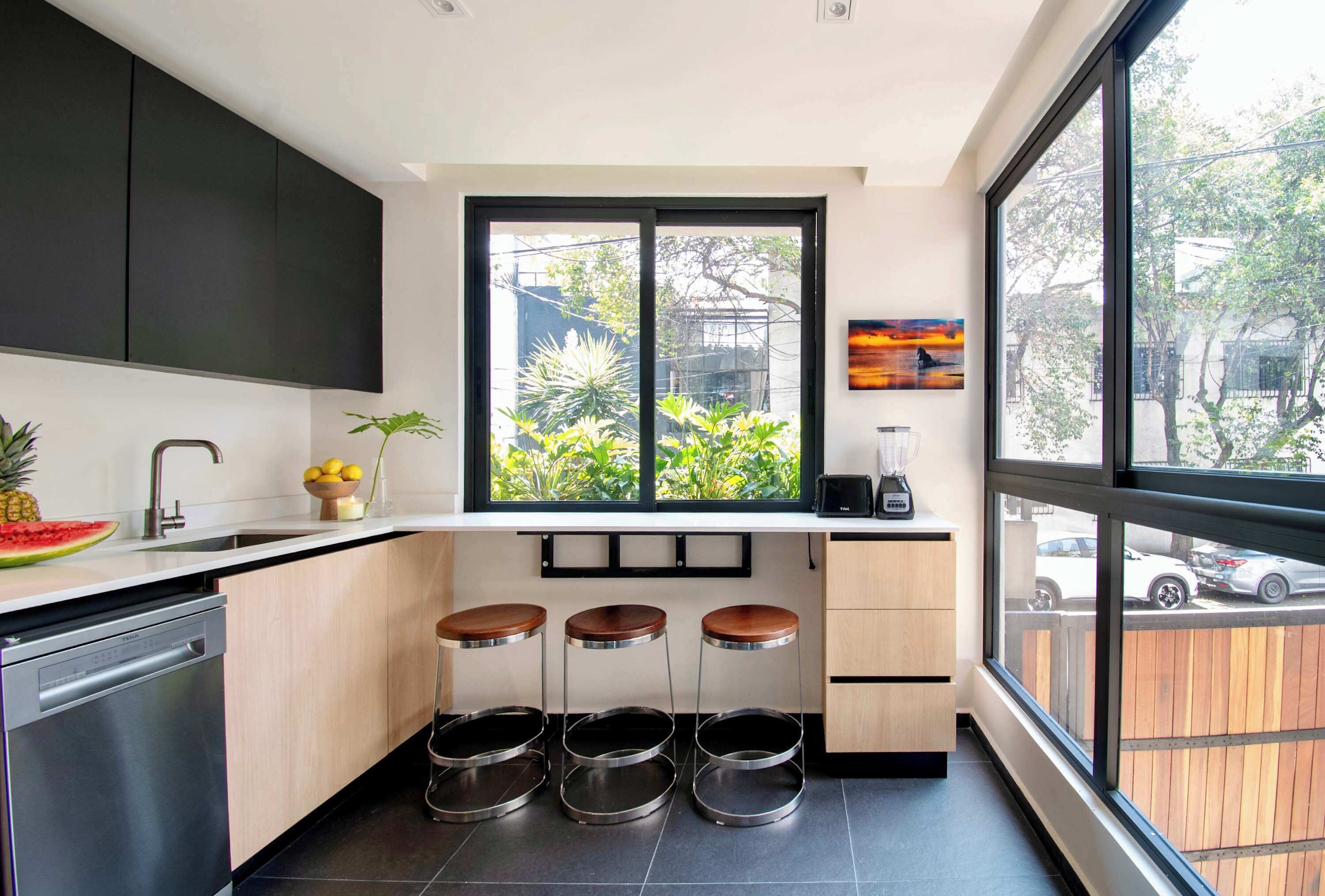 Cozinha moderna com lava-louças, pia, janela com vista para área verde e três banquetas.