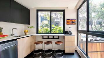Cozinha moderna com lava-louças, pia, janela com vista para área verde e três banquetas.