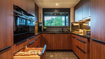 A modern kitchen with wooden cabinets, a built-in oven, and a window overlooking greenery.