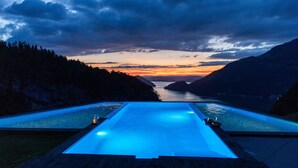 Ein Schwimmbad mit Holzterrasse, umgeben von Bergen und Blick auf einen Sonnenuntergang.
