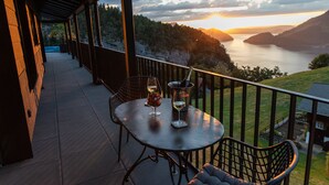 Ein überdachter Außenbereich mit Tisch und Stühlen, mit Blick auf ein Gewässer und Hügel.