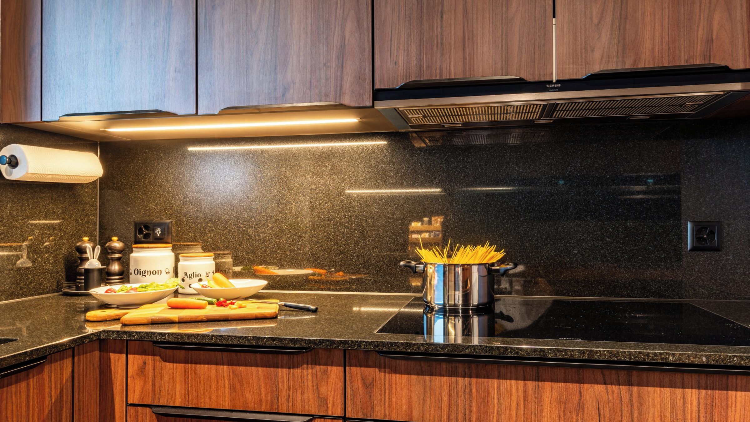 Une cuisine dotée d’un plan de travail noir, de meubles en bois, d’une hotte en acier inoxydable et de divers ustensiles de cuisine.