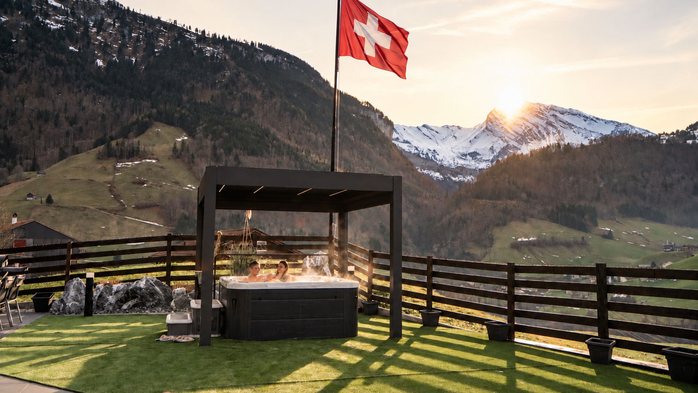 A hot tub with a Swiss flag, surrounded by a wooden fence, set against a mountainous backdrop.