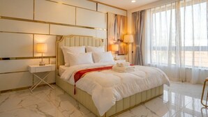 Ein Hotelzimmer mit einem großen Bett, Nachttischlampen, einem Nachttisch und Blick ins Freie durch transparente Vorhänge.