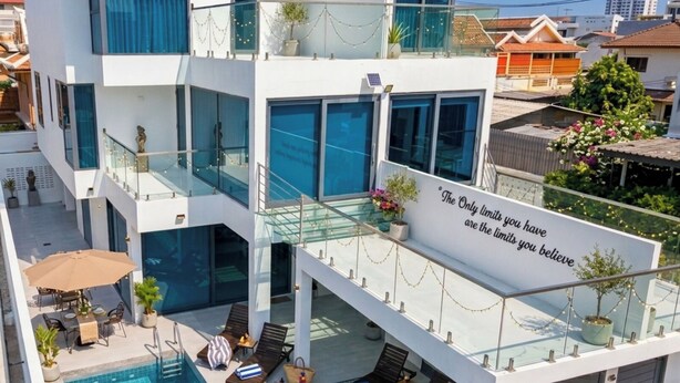 Ein modernes, mehrstöckiges Haus mit Pool, Außenbereich zum Sitzen und einem motivierenden Zitat am Balkon.