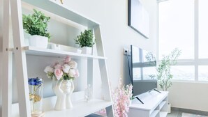 Una habitación moderna con una consola blanca, televisor y estanterías con plantas y flores.