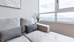 Ein modernes Wohnzimmer mit einer Couch, einer Pflanze und einem Fenster mit Blick auf die Stadt.