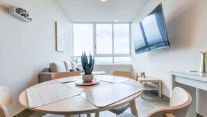 Ein modernes Wohnzimmer mit rundem Tisch, Sitzgelegenheiten, einem Flachbildfernseher, einer Pflanze und einem Fenster mit Blick.
