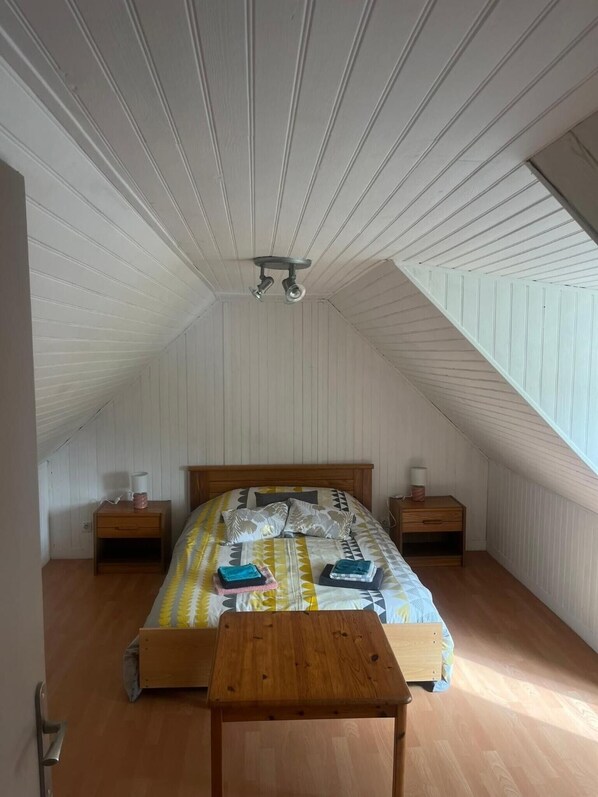A bedroom with a sloped ceiling, a bed with patterned bedding, two bedside tables with lamps, and a wooden bench.