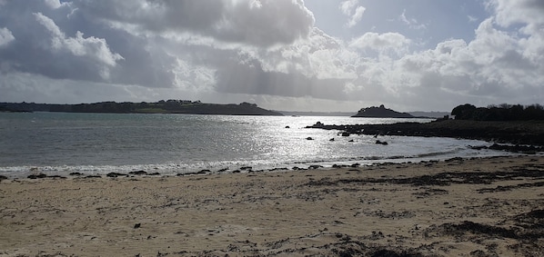 Ein Strand mit felsigem Ufer, ruhigem Wasser und sanften Hügeln im Hintergrund.