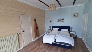 Una camera da letto con pavimento in legno, un letto con biancheria bianca, un lampadario a sospensione e una mensola a muro con oggetti decorativi.
