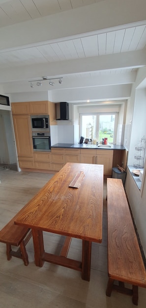 Eine moderne Küche mit Holzschränken, einem großen Holztisch und einem Fenster mit Blick ins Freie.
