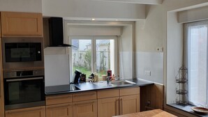 Una cucina con mobili in legno, un piano di lavoro nero, un forno in acciaio inossidabile, un forno a microonde e una finestra vista verde.