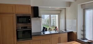 Eine Küche mit Holzschränken, einer schwarzen Arbeitsplatte, einem Edelstahlbackofen, einer Mikrowelle und einem Fenster mit Blick auf Grünflächen.