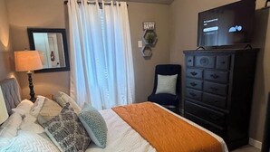 Une chambre à coucher avec un lit, une commode, un téléviseur et une chaise.