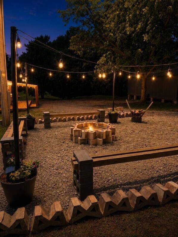 An outdoor patio area with a fire pit, string lights, and potted plants.