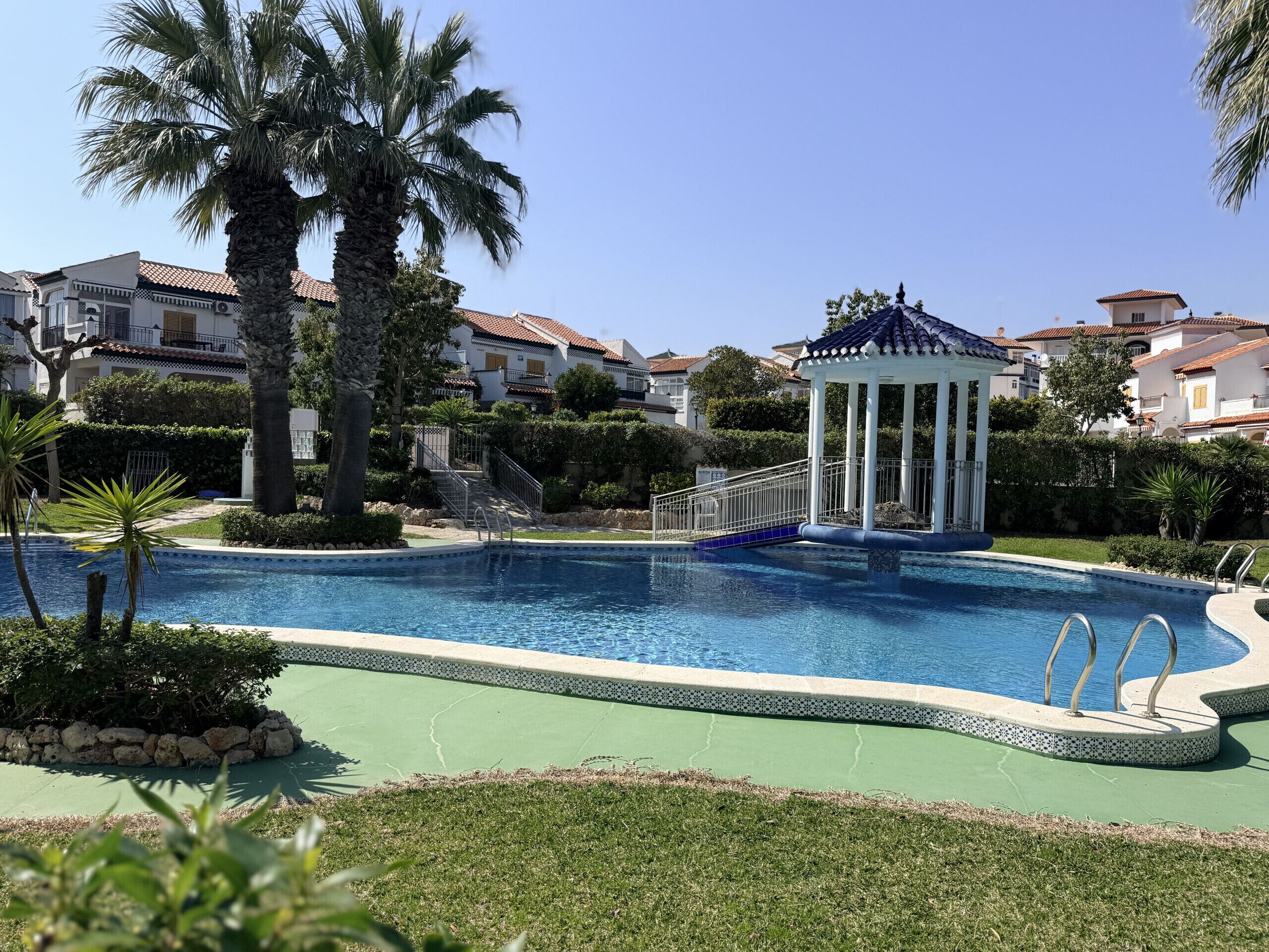 A swimming pool with a gazebo, palm trees, and a view of residential buildings.