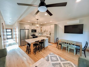 A modern kitchen with a central island, a dining area, and a ceiling fan. - The Kat's meow, 3-bedroom duplex in Nehalem (Nehalem)