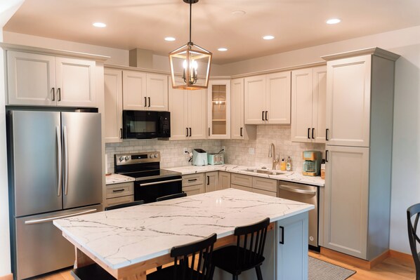 A modern kitchen with white cabinets, stainless steel appliances, a marble island, and a pendant light. - The Kat's meow, 3-bedroom duplex in Nehalem (Nehalem)