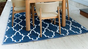 A patio with a wooden table and wicker chairs, a grill, and a blue patterned rug. - The Kat's meow, 3-bedroom duplex in Nehalem (Nehalem)