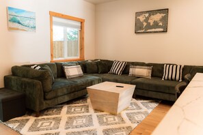 A living room with a sectional sofa, a coffee table, a patterned rug, a window with blinds, and a world map on the wall. - The Kat's meow, 3-bedroom duplex in Nehalem (Nehalem)